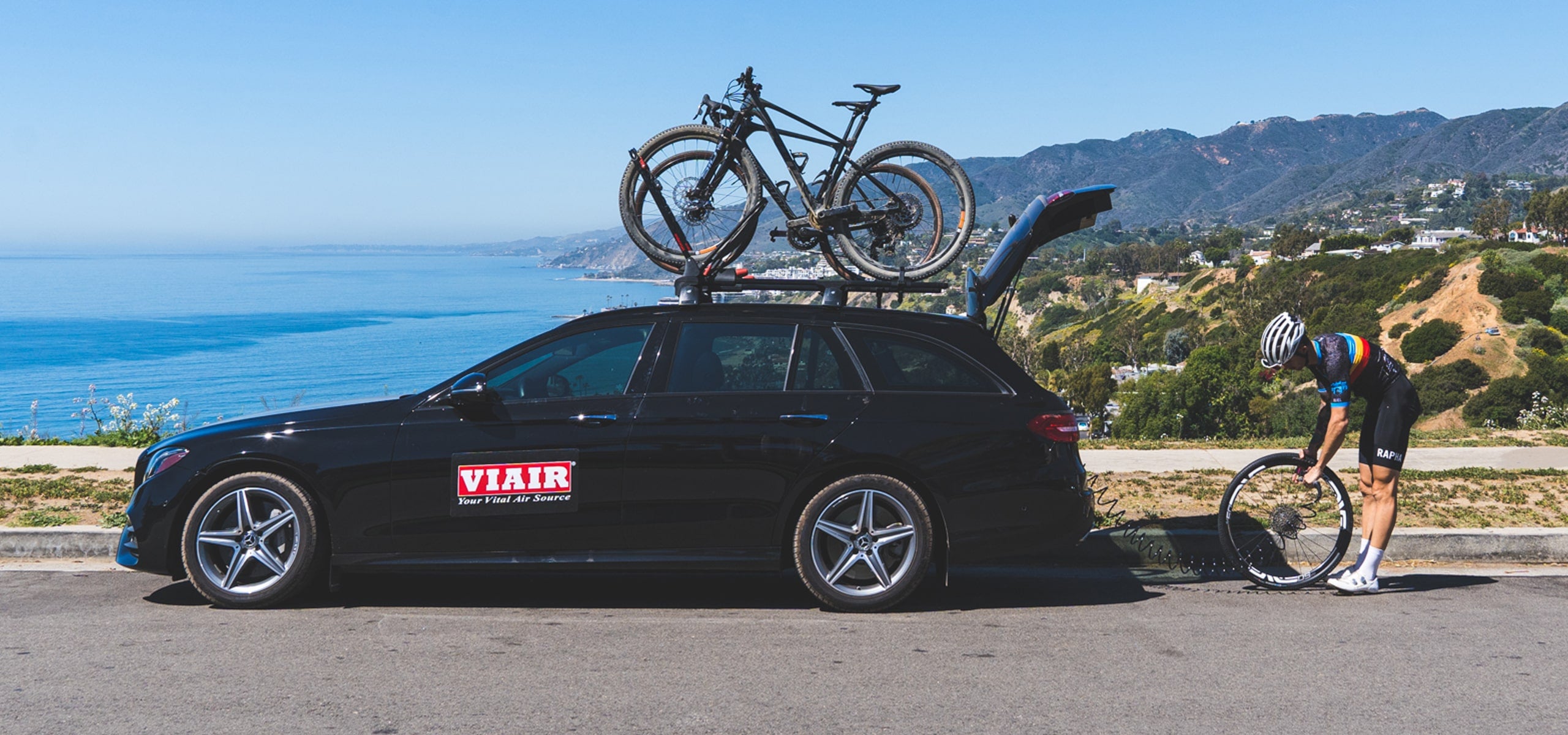 bikes on a car with a cyclist holding a wheel by the sea